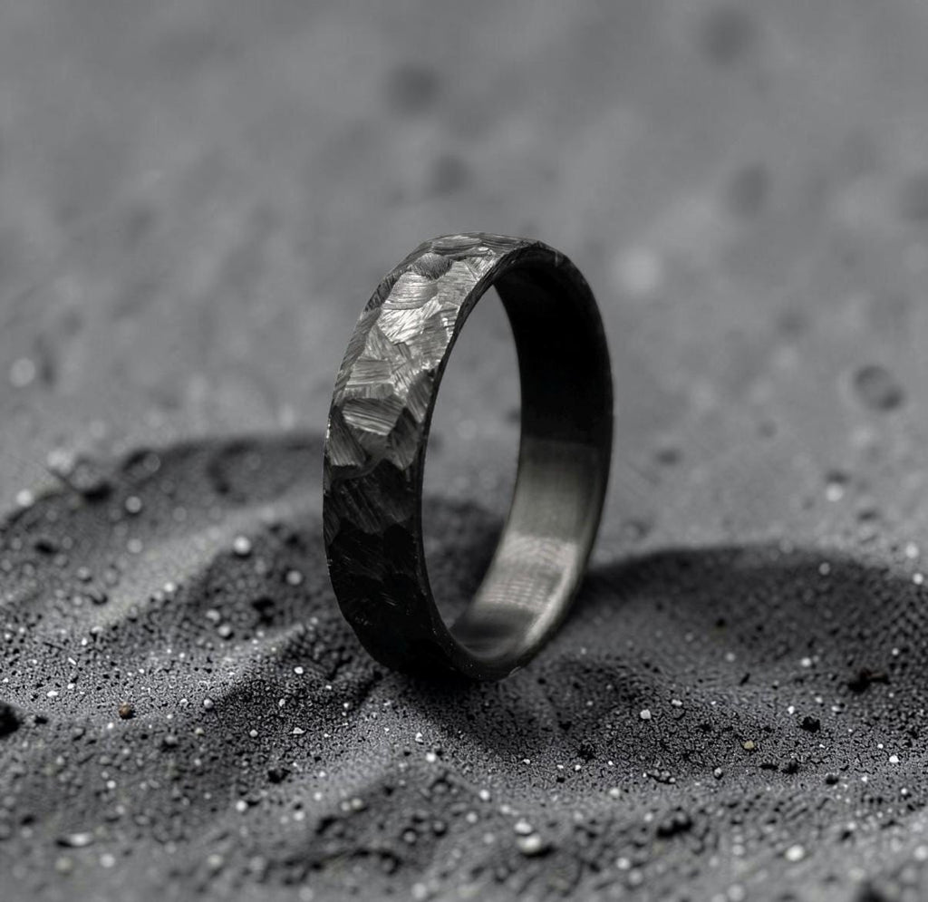Hand-forged zirconium wedding band with black hammered finish, standing upright on dark surface
