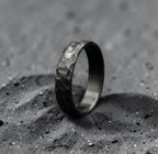 Hand-forged zirconium wedding band with black hammered finish, standing upright on dark surface