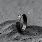 Minimalist black zirconium ring photographed at an angle against dark background