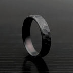 Black hammered zirconium ring standing on textured dark surface, front view