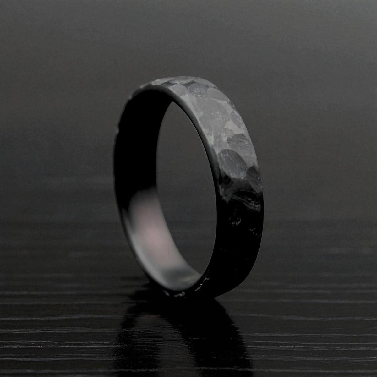 Black hammered zirconium ring standing on textured dark surface, front view