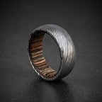 Damascus steel domed wedding band with dark wood inlay on dark surface