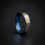 A brushed silver metal ring with a vibrant blue interior, standing upright on a dark, reflective surface.