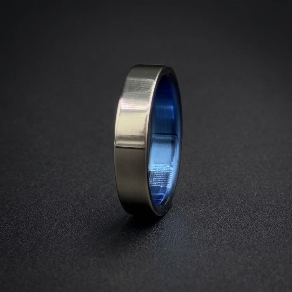 A brushed silver metal ring with a vibrant blue interior, standing upright on a dark textured surface.