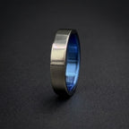A brushed silver metal ring with a vibrant blue interior, standing upright on a dark textured surface.