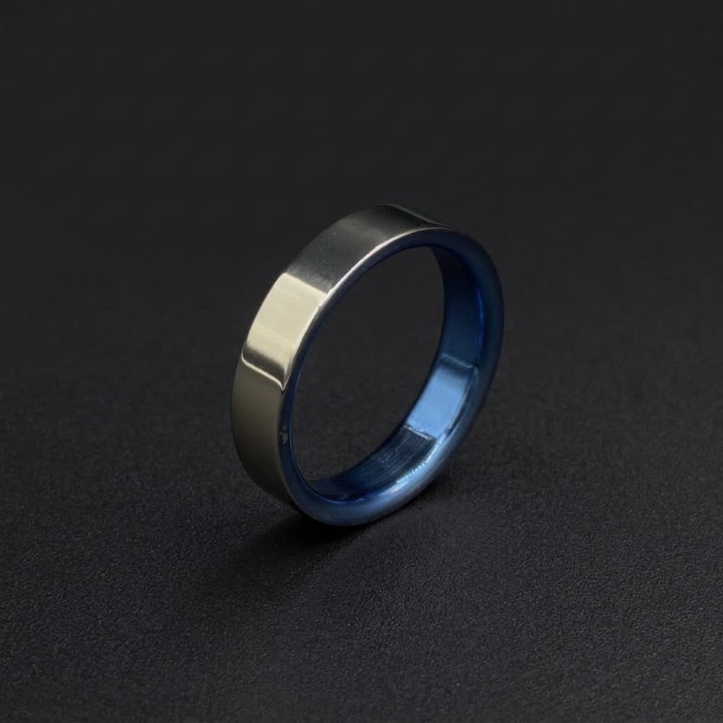 A minimalist metal ring with a brushed silver exterior and a polished blue interior, standing upright on a dark textured surface.