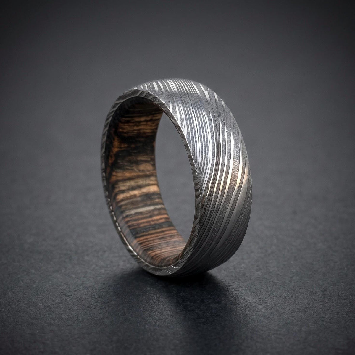 Close-up detail of etched Damascus steel layers on domed wood inlay ring