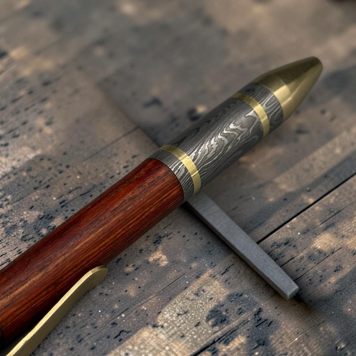 Damascus steel pen shown at an angle showing forged copper clip