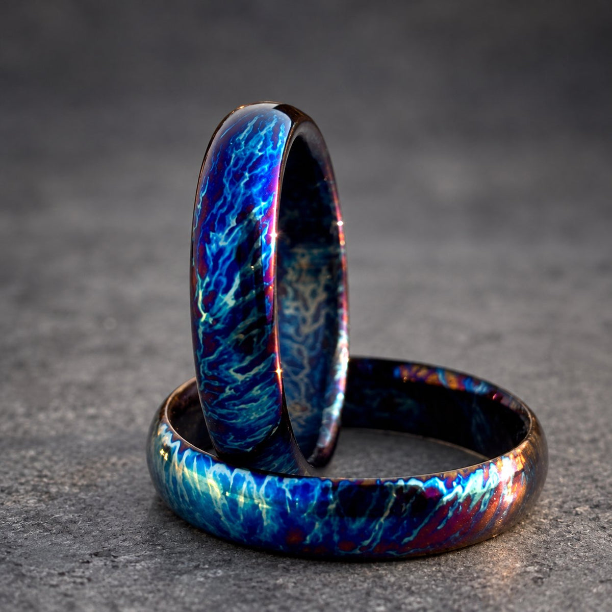 Two matching rings with a blue, purple and black iridescent finish. The rings are stacked on top of each other.