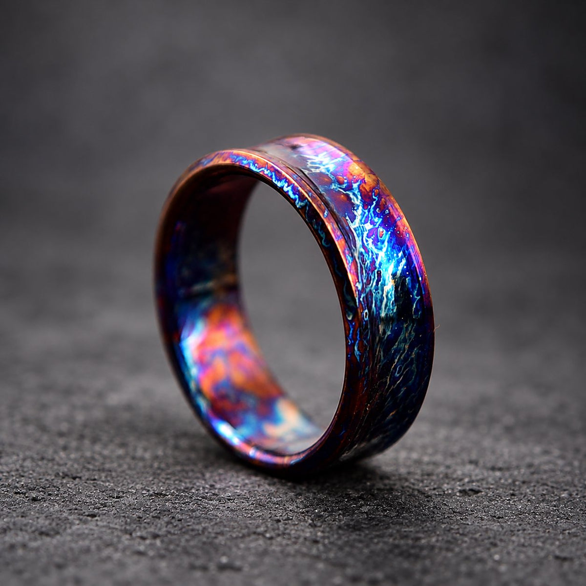 A close-up of a colorful, iridescent ring with a wide band. The ring is made of metal and has a unique, swirling pattern.