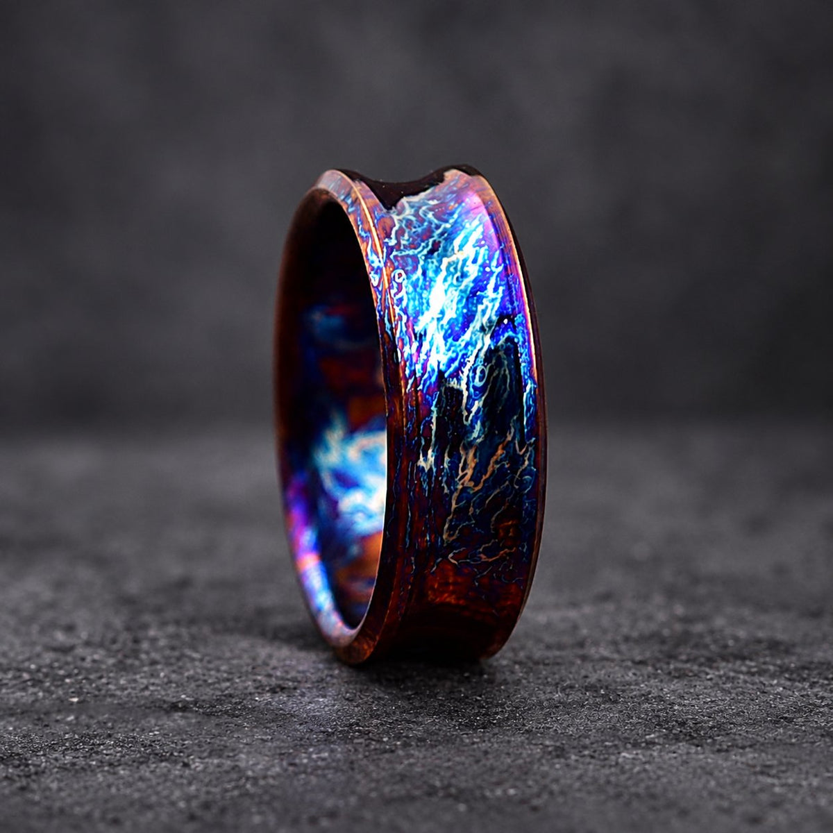 A close-up of a dark blue and purple ring with a beveled edge and a swirling pattern. The ring is made of metal and has a unique, iridescent finish.