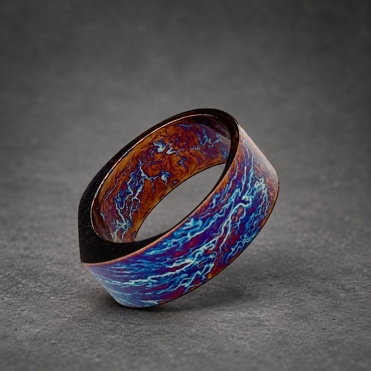 A wide, dark blue and copper ring with a swirling, marbled pattern. The ring is made of metal and has a smooth, polished finish.