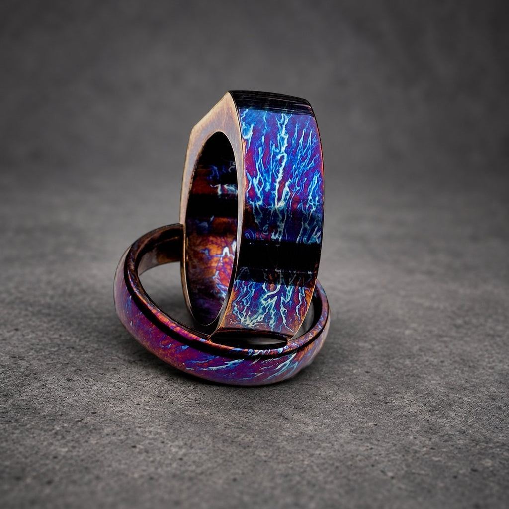 Two stacked rings with a blue and purple iridescent finish. The rings are made of metal and have a unique, swirling pattern.