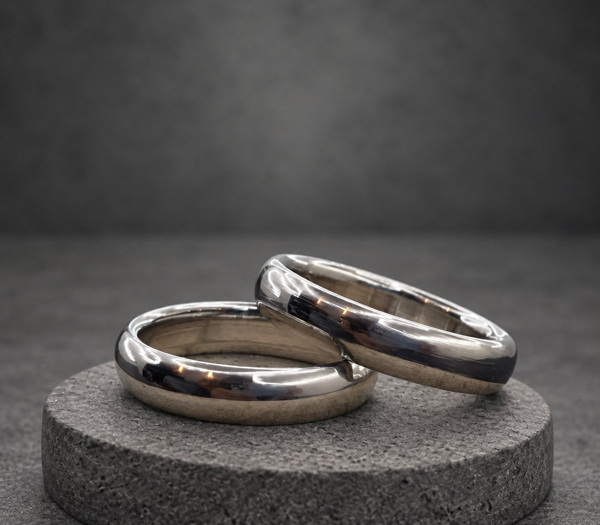 Two silver wedding bands, one slightly larger than the other, are stacked on top of each other on a wooden surface.