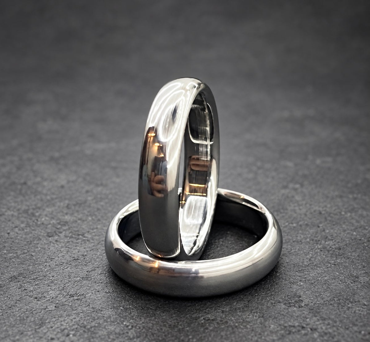 Two silver wedding bands stacked on top of each other. The top band has a polished finish and the bottom band has a brushed finish.