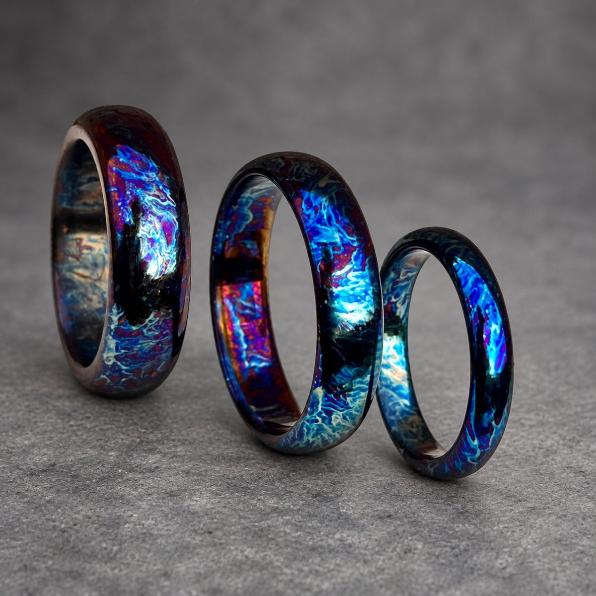Three iridescent rings with a blue, purple and black color scheme. The rings are stacked on top of each other, with the largest ring on the bottom and the smallest ring on top.