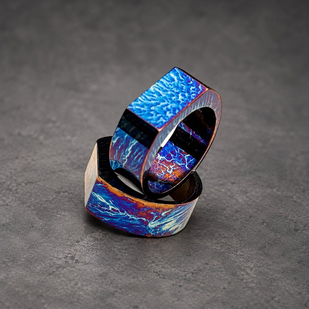 Two stacked rings with a blue and purple iridescent finish. The rings are made of metal and have a square shape.