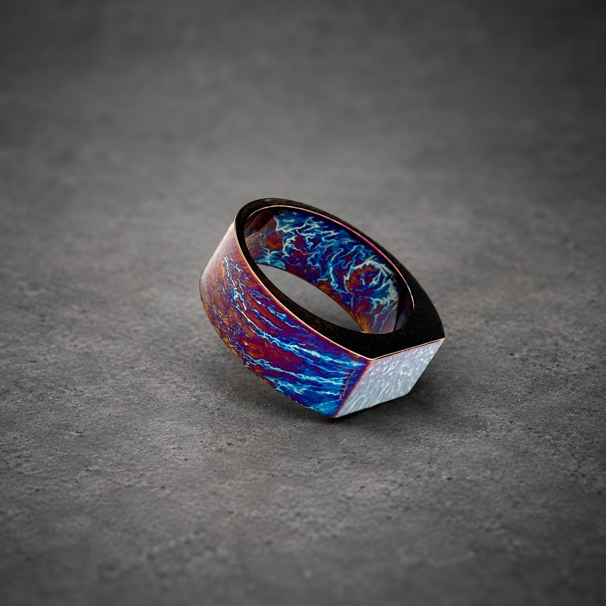 A wide, flat ring with a blue, purple and red marbled pattern. The ring is made of metal and has a square-shaped top.