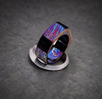 A hexagonal shaped ring with a blue, purple and red iridescent finish. The ring is sitting on a silver surface.