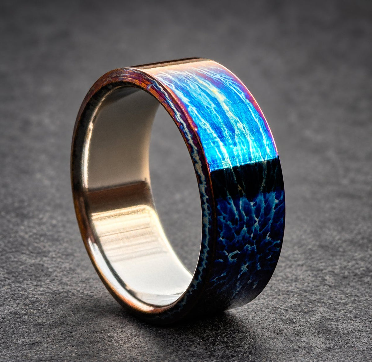 A blue and black ring with a textured finish. The ring is made of metal and has a wide band.