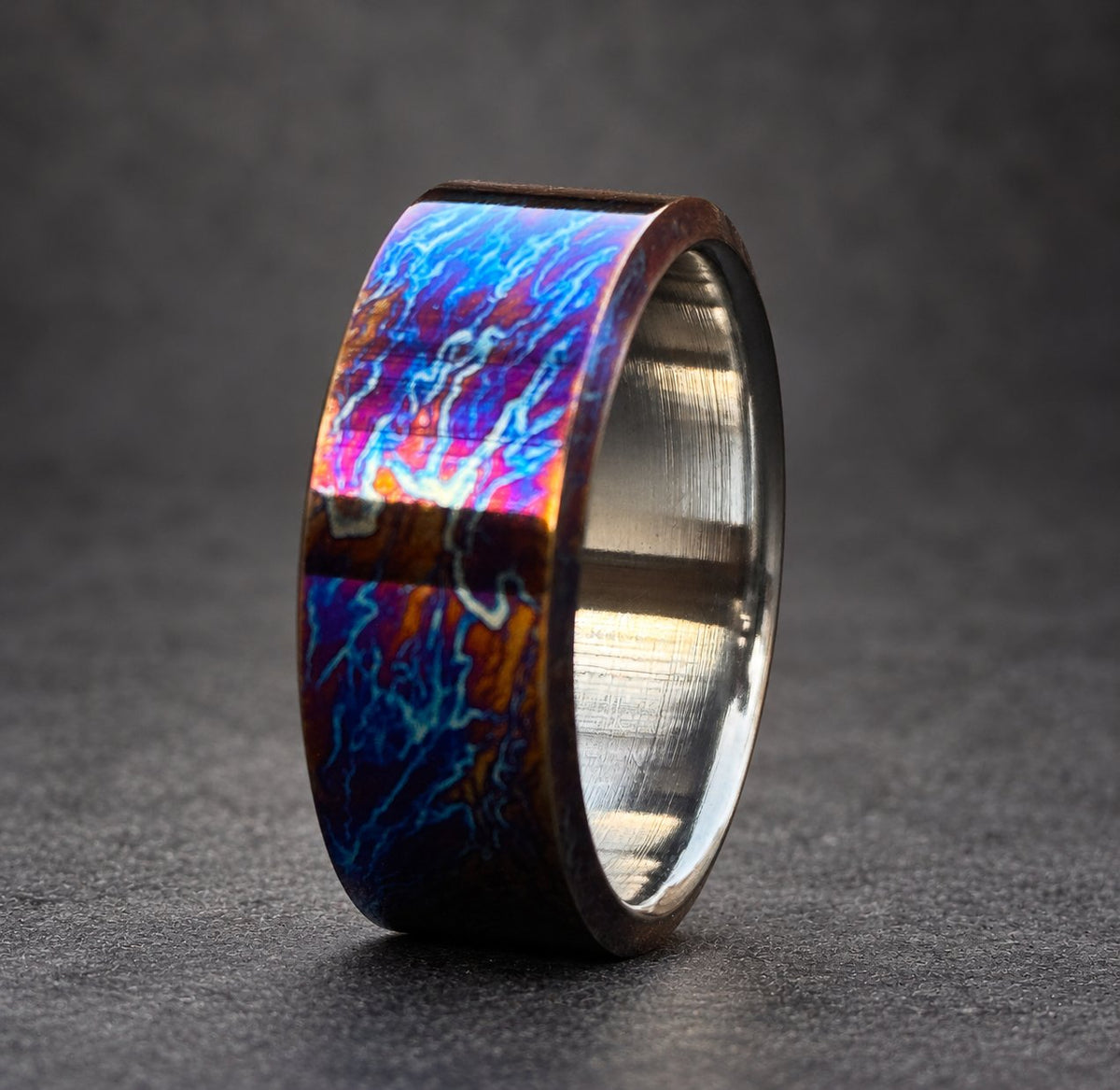 A wide, silver band with a blue, purple and orange iridescent finish. The band has a smooth, polished surface.