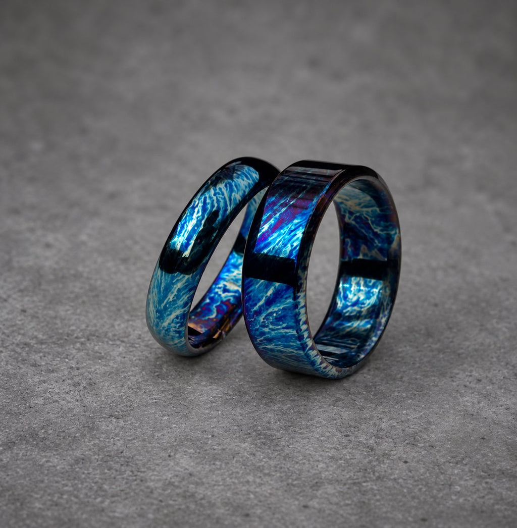Two blue and black patterned rings, one slightly larger than the other, are stacked together. The rings have a metallic finish and a swirling pattern.