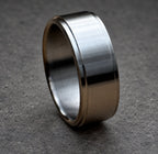 A brushed metal ring with a flat top and bottom, and a slightly rounded edge. The ring has a simple, minimalist design and a matte finish. The ring is shown on a neutral background.