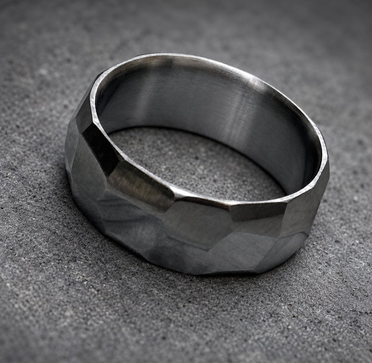 A dark gray hammered metal ring with a wide band.