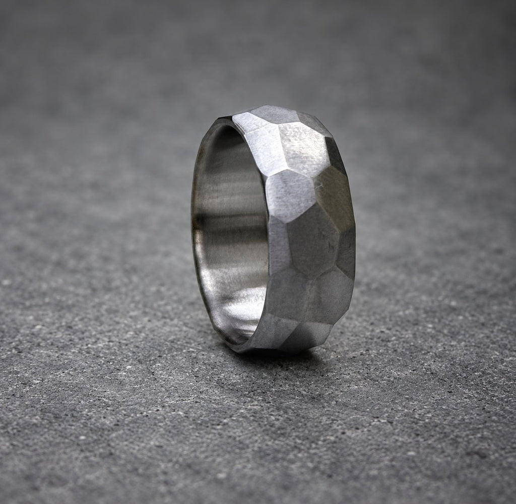 A silver ring with a textured, faceted design. The ring is made of metal and has a polished finish.