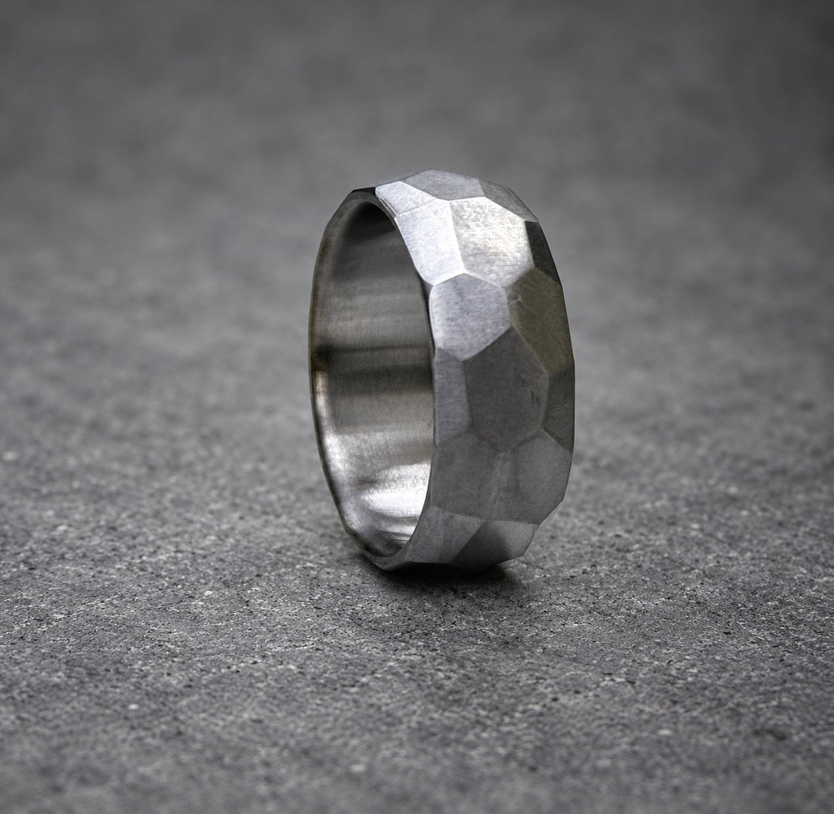 A silver ring with a textured, faceted design. The ring is made of metal and has a polished finish.