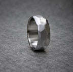 A silver ring with a textured, faceted design. The ring is made of metal and has a polished finish.