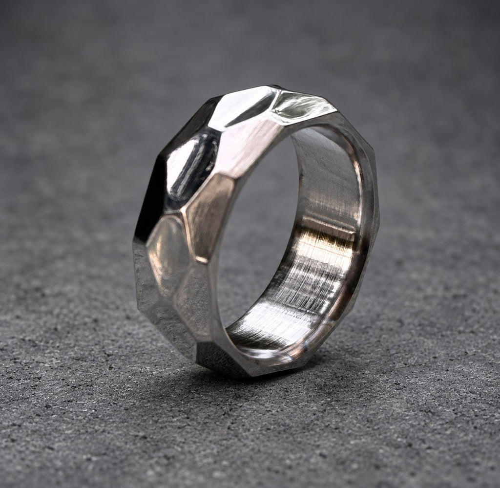 A silver ring with a faceted, geometric design. The ring is made of metal and has a brushed finish.