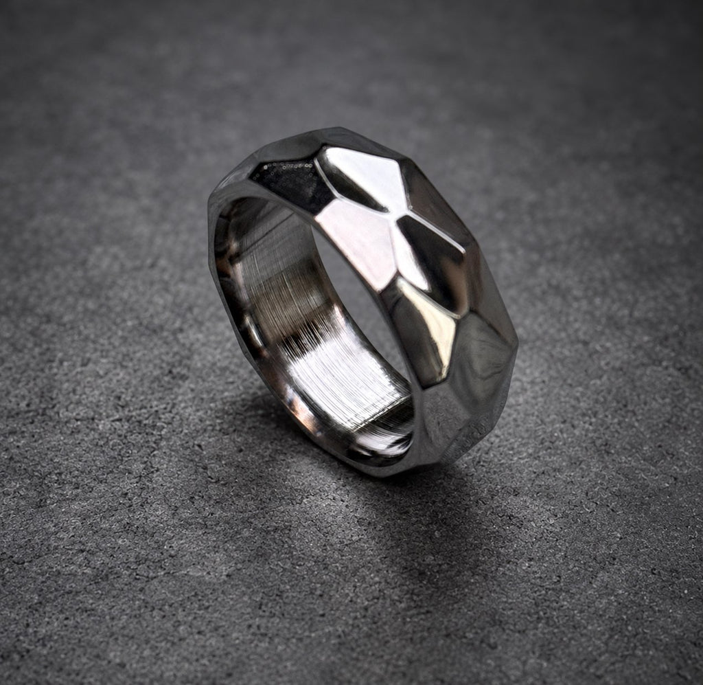 A silver ring with a geometric, faceted design. The ring is made of brushed metal and has a shiny finish.