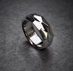 A silver ring with a geometric, faceted design. The ring is made of brushed metal and has a shiny finish.