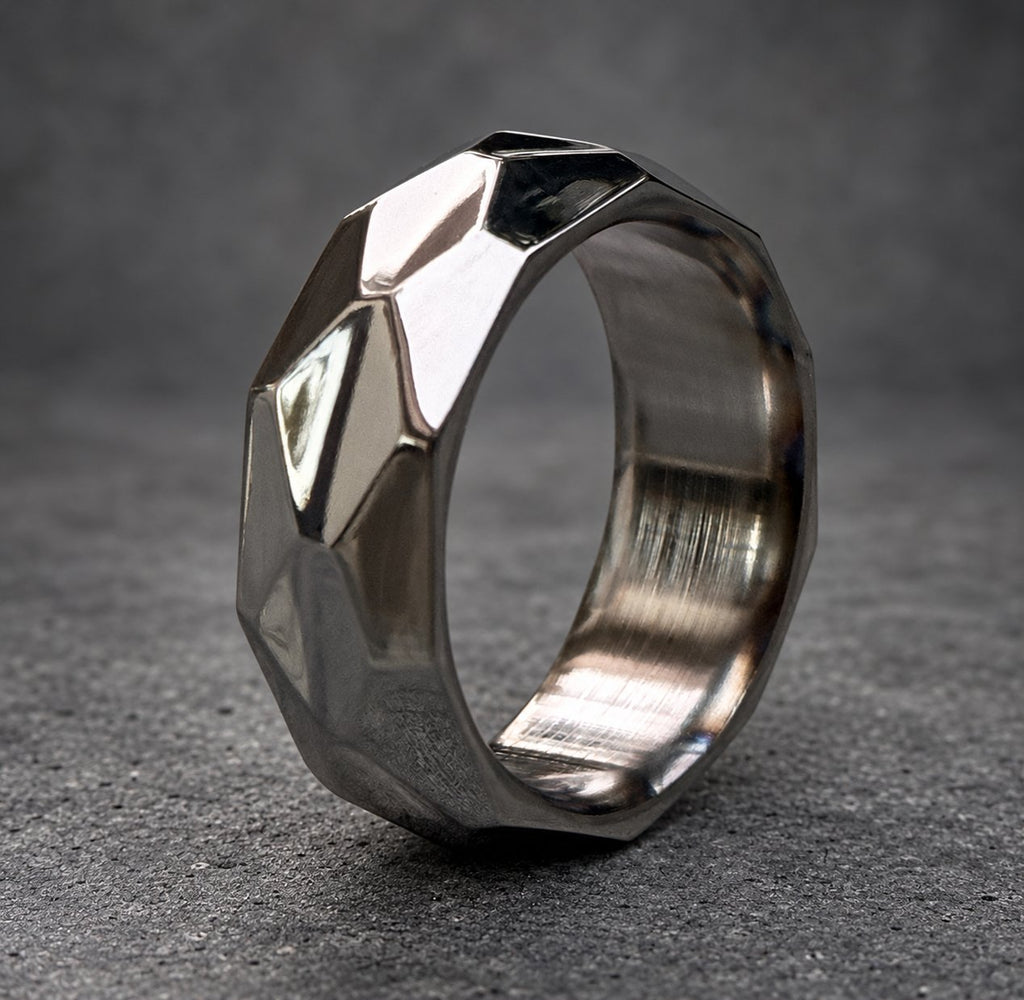 A silver ring with a geometric, faceted design. The ring is made of metal and has a brushed finish, view 2