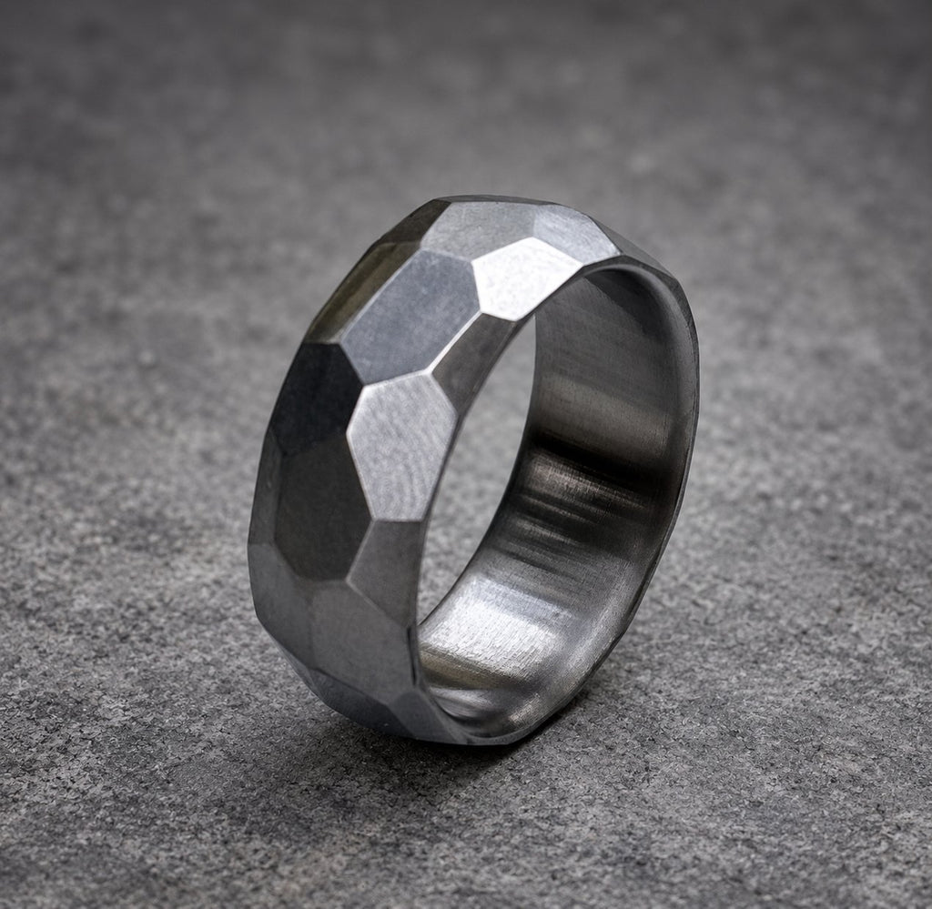 A silver ring with a faceted, geometric design. The ring is made of metal and has a brushed finish.