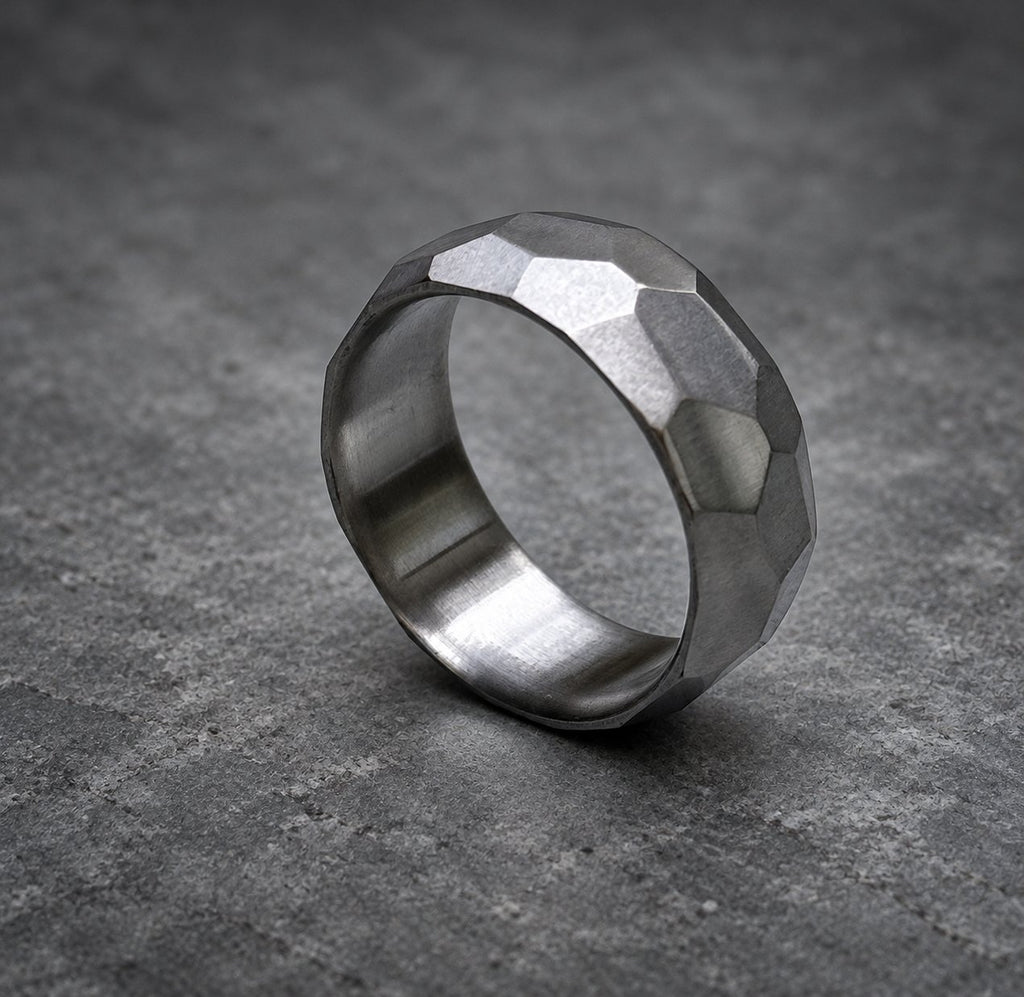 A silver ring with a textured, faceted design. The ring is made of metal and has a polished finish, view 3