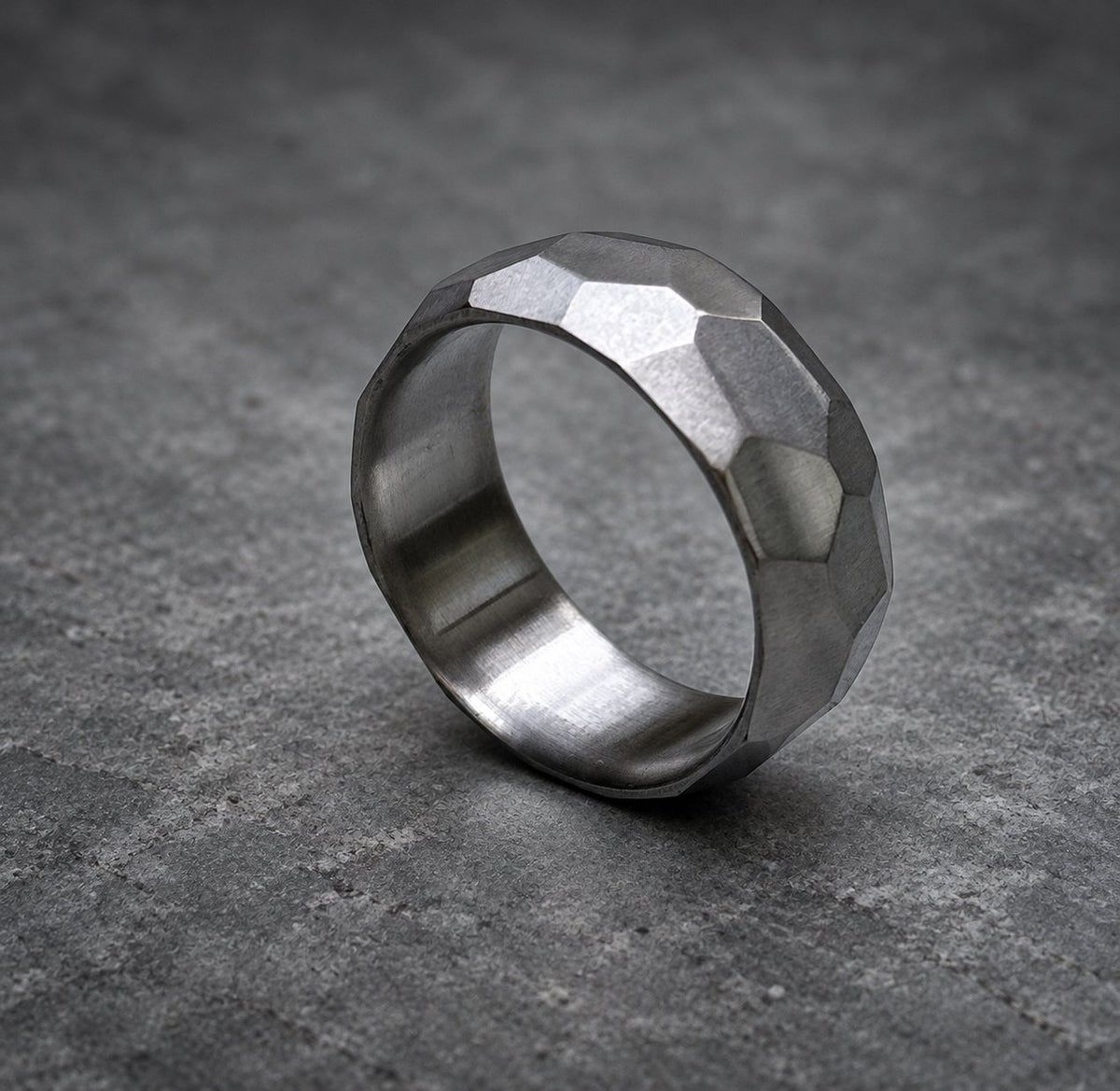 A silver ring with a textured, faceted design. The ring is made of metal and has a polished finish, view 3