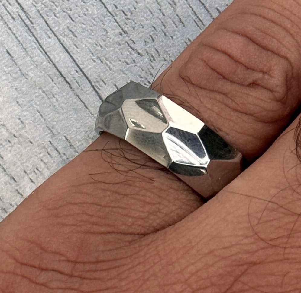 A silver ring with a geometric, faceted design. The ring is worn on a finger.