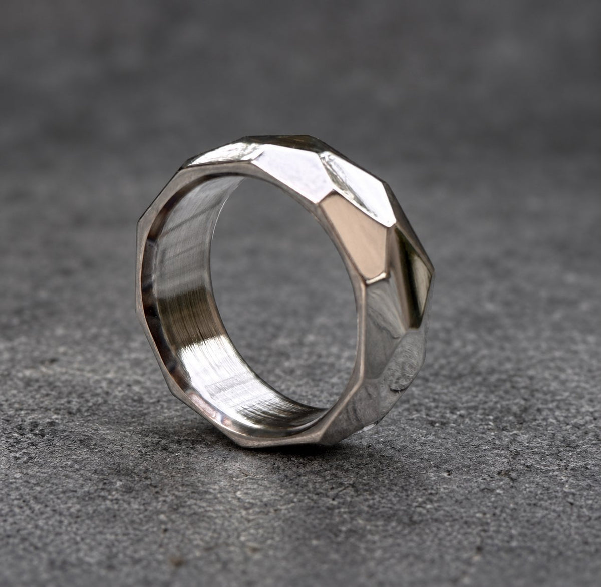 A silver ring with a faceted, geometric design. The ring is made of metal and has a brushed finish, view 5