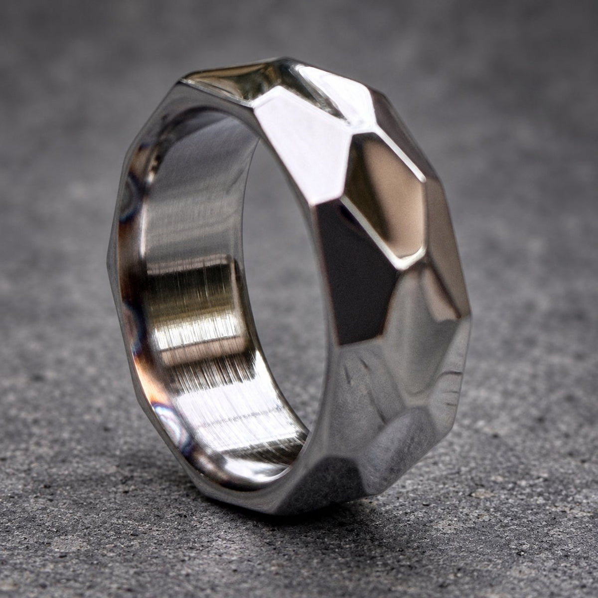 A silver ring with a geometric, faceted design. The ring is made of metal and has a brushed finish.