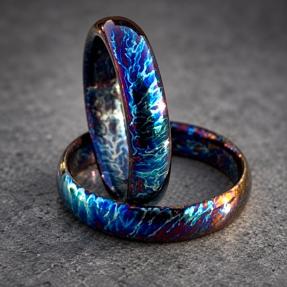 Two matching wedding bands with a blue and purple iridescent finish. The bands are made of metal and have a smooth, polished surface.
