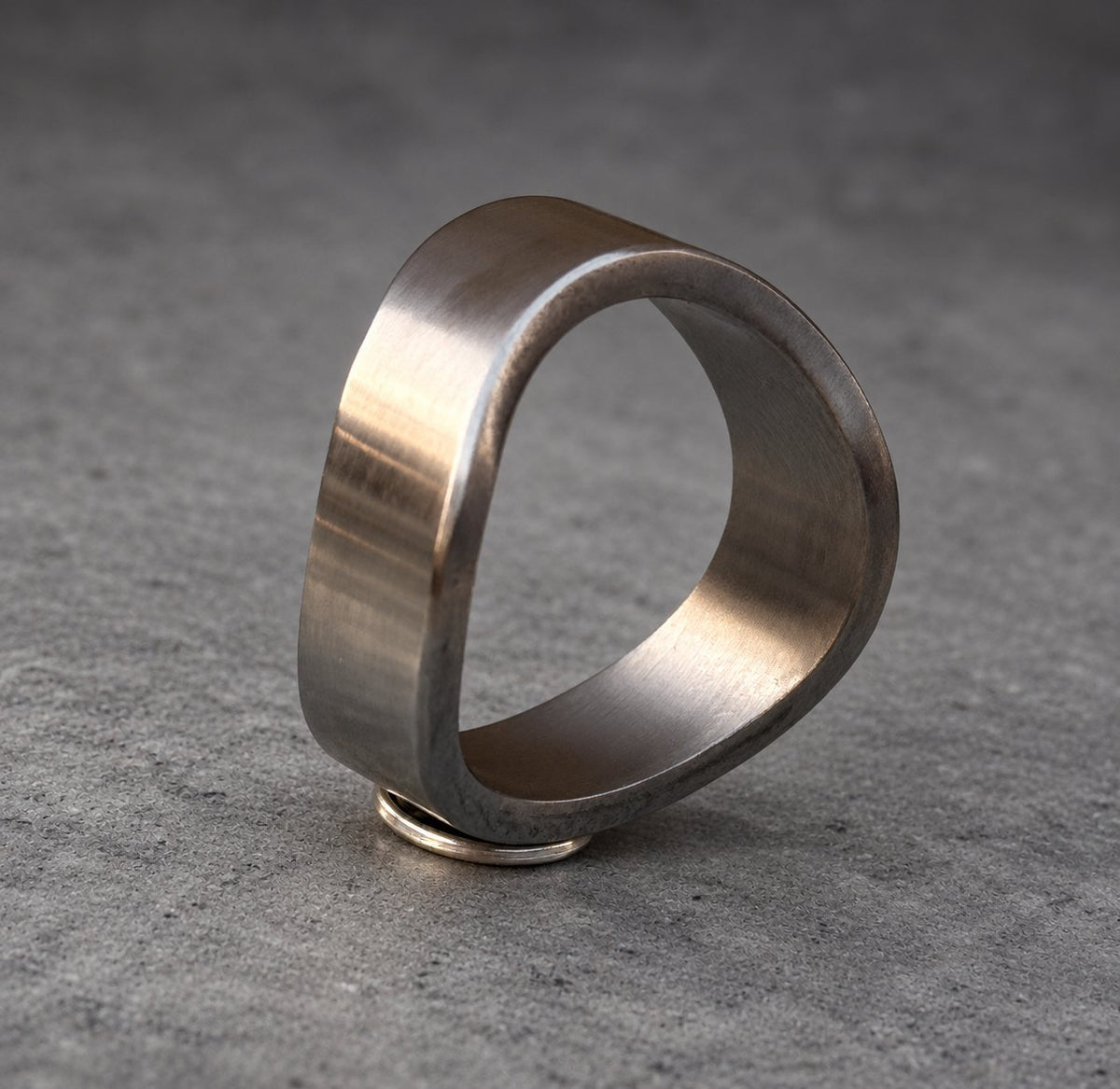 A silver ring with a unique, asymmetrical design. The ring is made of metal and has a smooth, polished finish.
