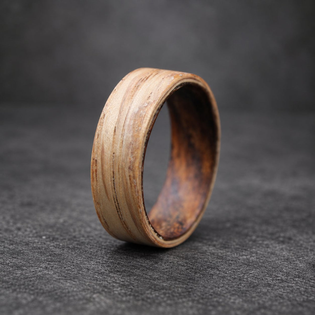 A wooden ring with a natural wood grain finish. The ring is made of multiple layers of wood, creating a unique pattern. The ring is brown and has a smooth, polished surface.
