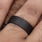 A dark brown wooden ring with a smooth, polished finish. The ring is worn on a finger.