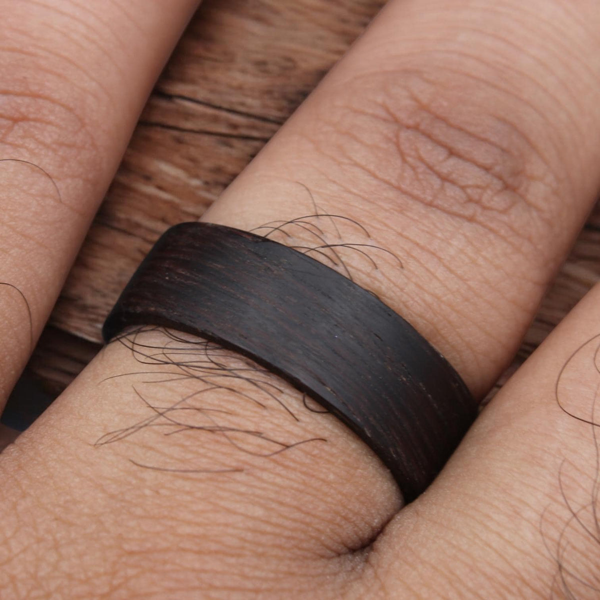A dark brown wooden ring with a smooth, polished finish. The ring is worn on a finger.