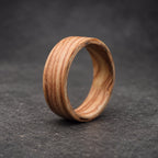 A wooden ring with a natural wood grain pattern. The ring is made of a light brown wood with darker brown streaks.