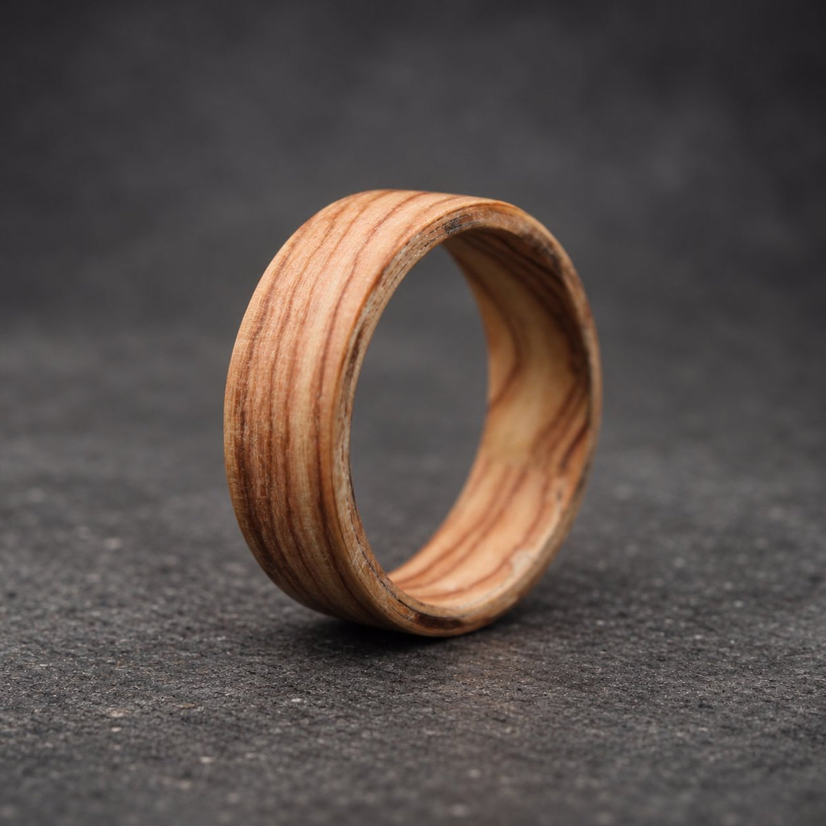 A wooden ring with a natural wood grain pattern. The ring is made of a light brown wood with darker brown streaks.