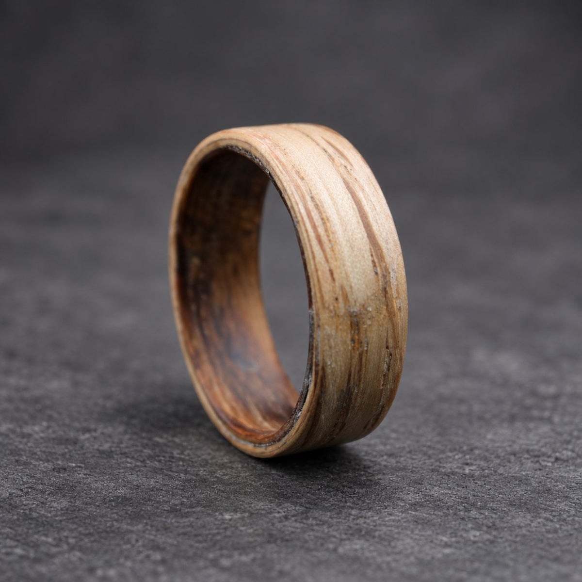 A wooden ring with a light brown outer layer and a dark brown inner layer. The ring is made of wood and has a natural grain pattern.