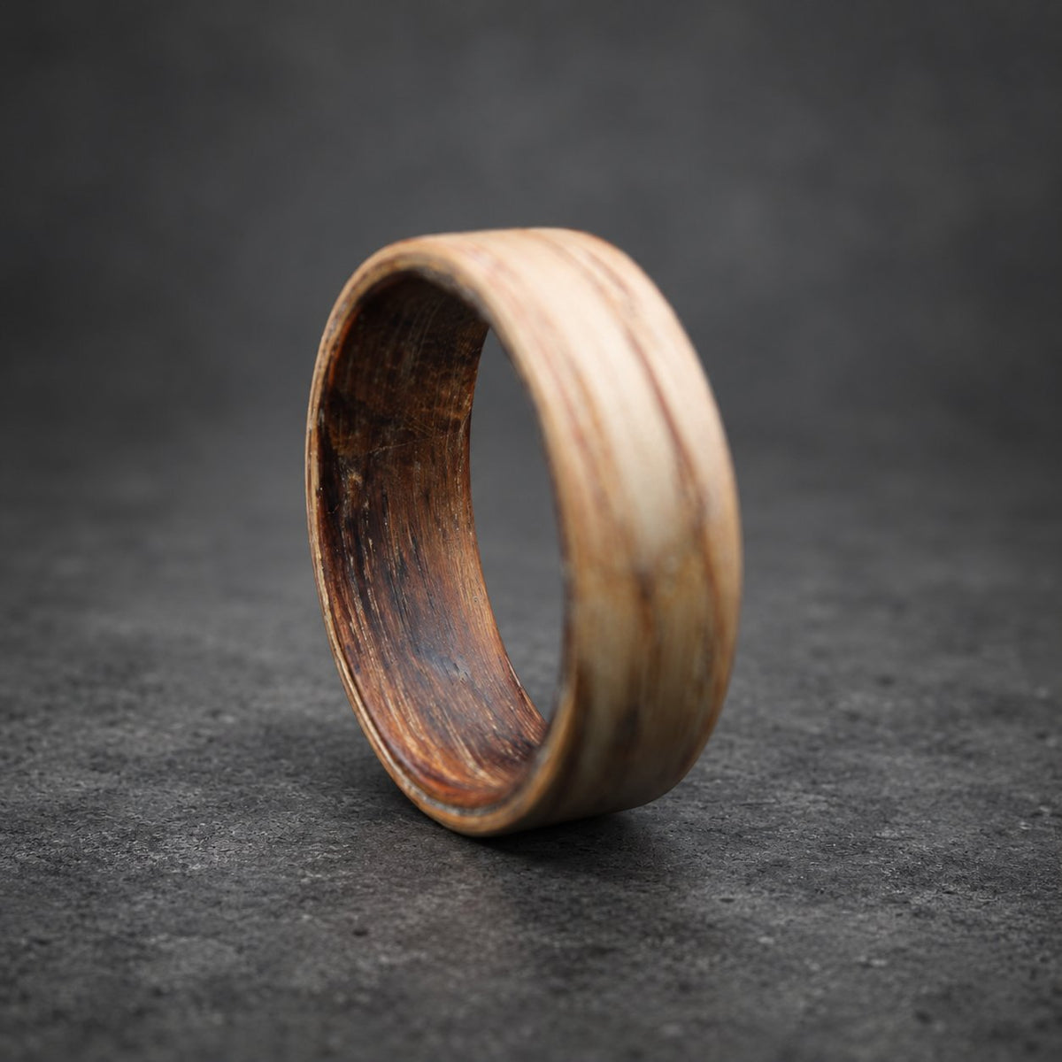 A wooden ring with a dark brown inner band and a light brown outer band. The ring is made of wood and has a natural finish.